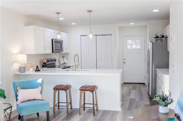 kitchen featuring pendant lighting, white cabinets, light hardwood / wood-style floors, kitchen peninsula, and stainless steel appliances