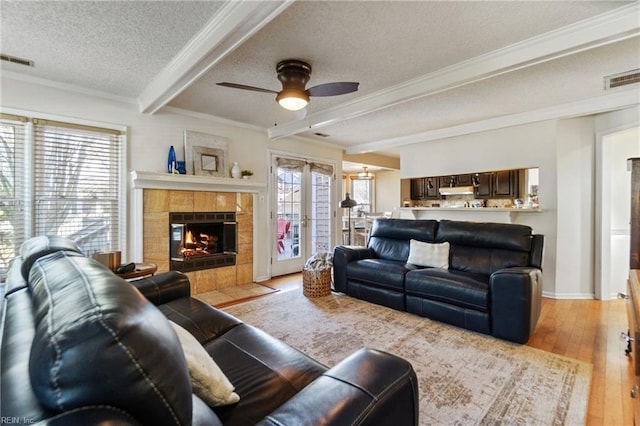 living room featuring beamed ceiling, a healthy amount of sunlight, a textured ceiling, and light wood-type flooring