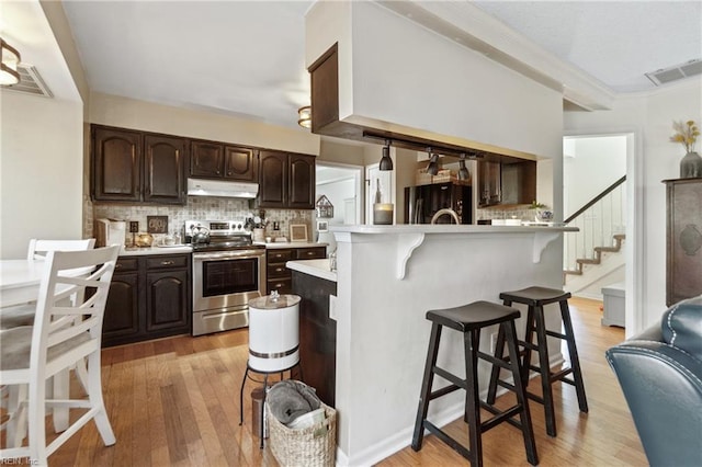 kitchen featuring a breakfast bar, black refrigerator, backsplash, dark brown cabinets, and stainless steel electric stove