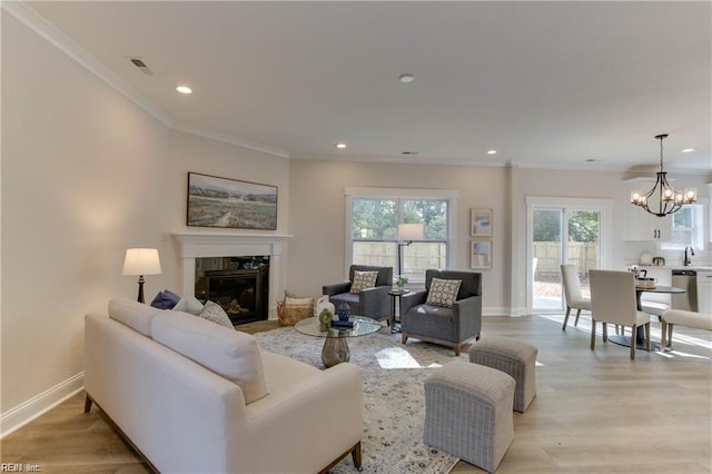 living room with sink, light hardwood / wood-style flooring, a chandelier, a fireplace, and ornamental molding