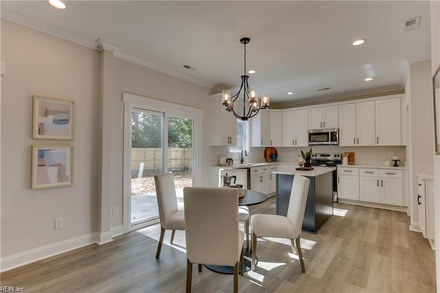 dining space featuring light hardwood / wood-style floors, ornamental molding, sink, and an inviting chandelier