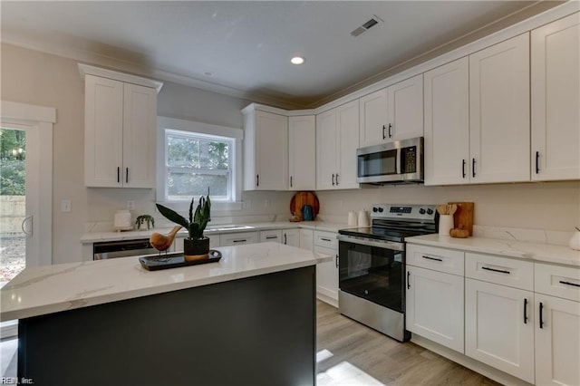 kitchen with light hardwood / wood-style floors, light stone counters, white cabinetry, and appliances with stainless steel finishes