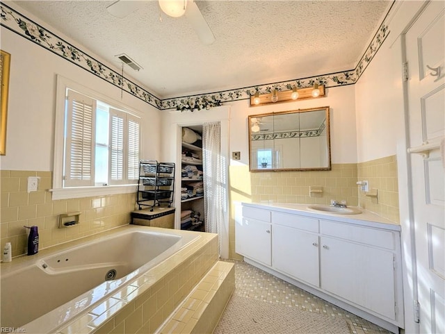 bathroom with tile patterned floors, a textured ceiling, tile walls, vanity, and a relaxing tiled tub