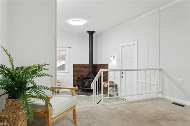 living area featuring visible vents, baseboards, carpet, a wood stove, and crown molding