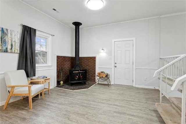 sitting room with visible vents, ornamental molding, a wood stove, wood finished floors, and stairs