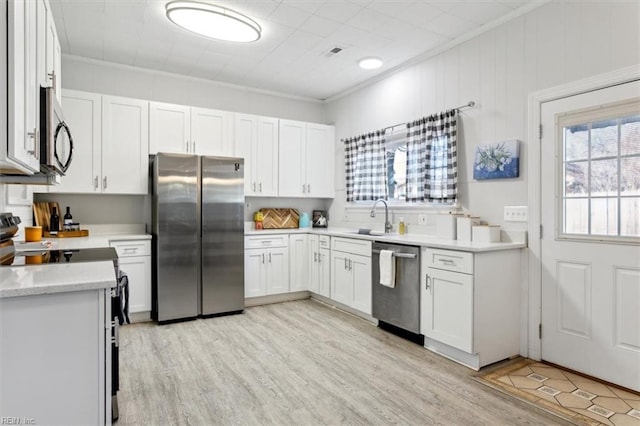 kitchen featuring stainless steel appliances, a sink, white cabinetry, light wood-style floors, and light countertops