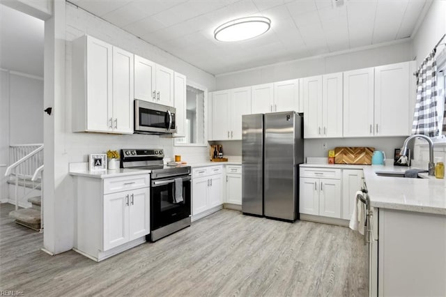 kitchen with light stone counters, a sink, white cabinetry, appliances with stainless steel finishes, and light wood-type flooring