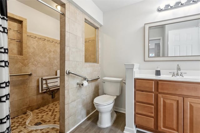 bathroom featuring toilet, wood finished floors, tiled shower, and vanity