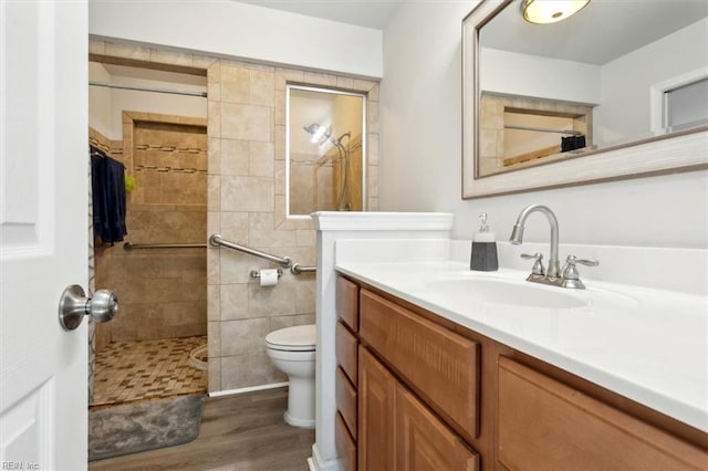 bathroom with a tile shower, vanity, toilet, and wood finished floors