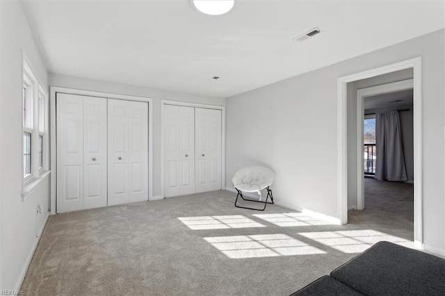 unfurnished bedroom featuring carpet floors, baseboards, visible vents, and multiple closets