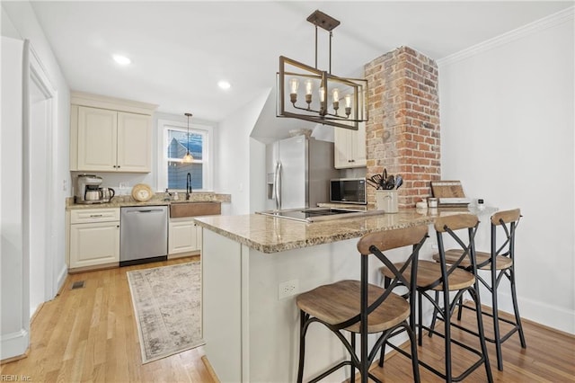 kitchen featuring stainless steel appliances, sink, light wood-type flooring, hanging light fixtures, and light stone countertops