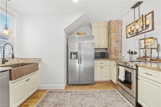 kitchen with stainless steel appliances, sink, cream cabinets, light hardwood / wood-style floors, and hanging light fixtures