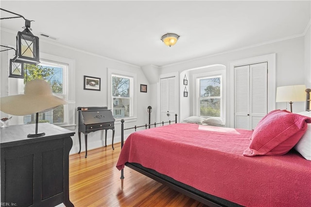 bedroom featuring two closets, crown molding, and hardwood / wood-style flooring