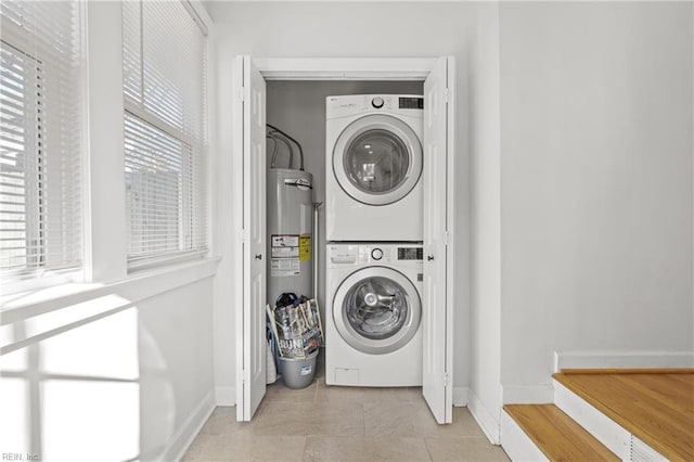 clothes washing area with stacked washer / drying machine, light tile patterned floors, and electric water heater