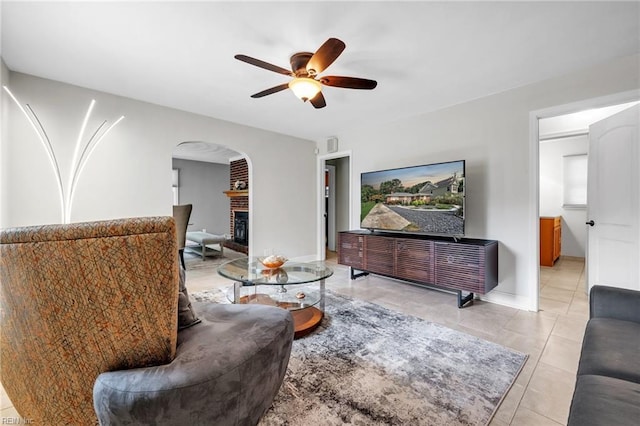 living room featuring ceiling fan, light tile patterned floors, and a brick fireplace