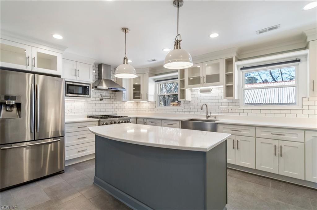 kitchen with appliances with stainless steel finishes, sink, wall chimney range hood, white cabinets, and a kitchen island