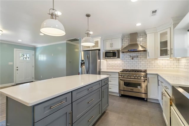 kitchen featuring pendant lighting, backsplash, white cabinets, wall chimney range hood, and appliances with stainless steel finishes