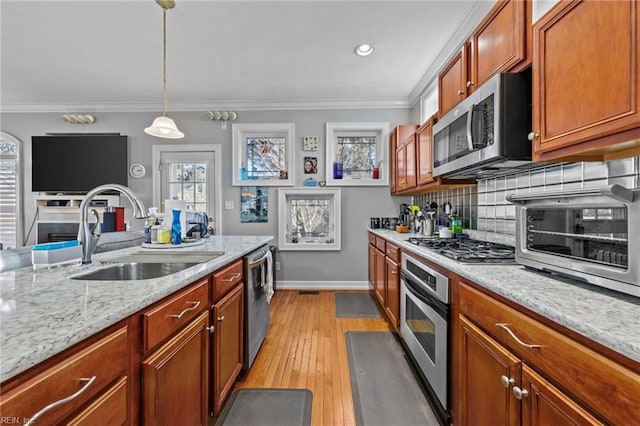 kitchen featuring sink, hanging light fixtures, stainless steel appliances, light stone counters, and ornamental molding