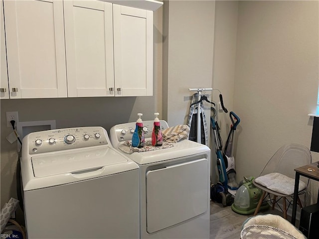 clothes washing area with wood finished floors, washing machine and clothes dryer, and cabinet space