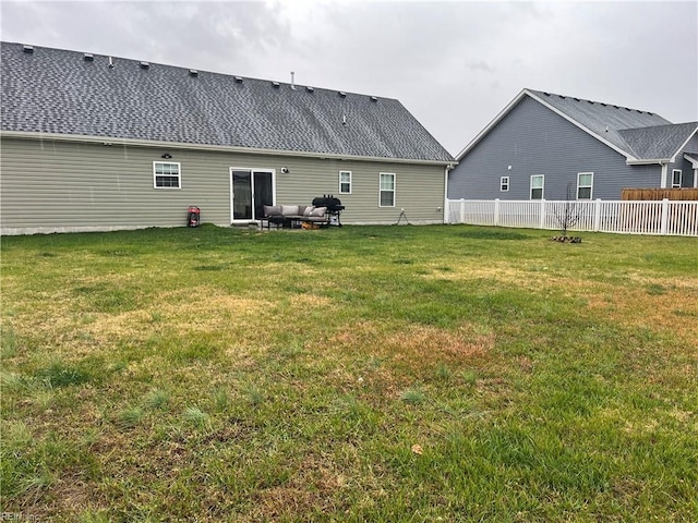 rear view of house featuring roof with shingles, a lawn, and fence