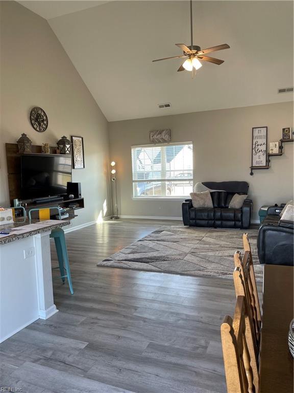 living area with high vaulted ceiling, a ceiling fan, visible vents, and wood finished floors