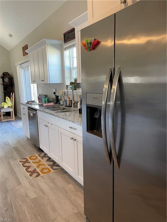 kitchen with stainless steel appliances, lofted ceiling, white cabinetry, and light stone counters