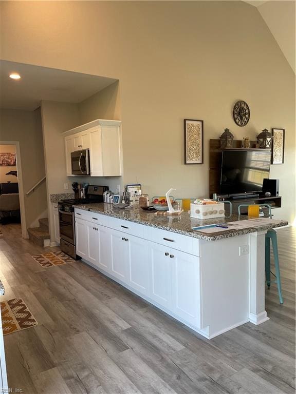 kitchen with light stone counters, light wood finished floors, appliances with stainless steel finishes, white cabinetry, and a kitchen bar