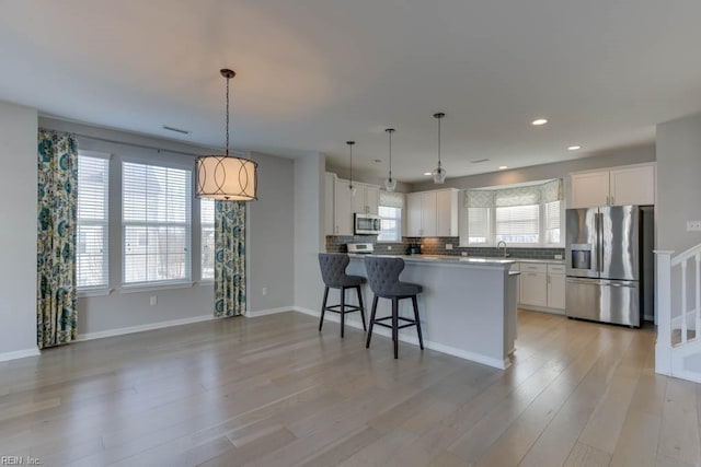 kitchen with white cabinetry, a kitchen bar, kitchen peninsula, appliances with stainless steel finishes, and hanging light fixtures