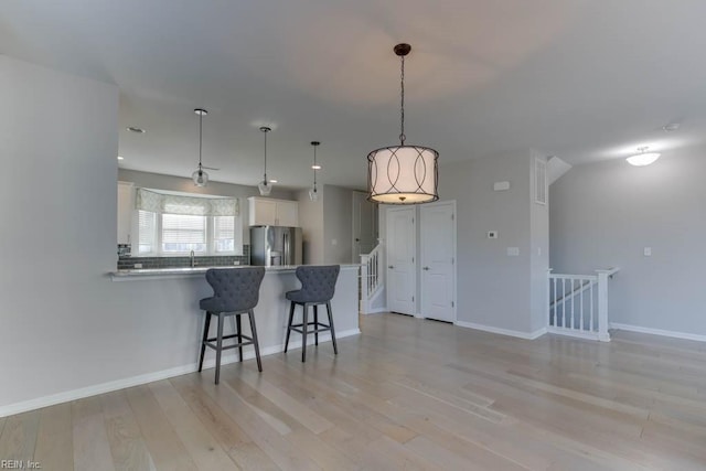 kitchen with stainless steel refrigerator with ice dispenser, white cabinetry, a kitchen breakfast bar, hanging light fixtures, and kitchen peninsula