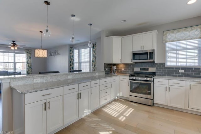 kitchen with kitchen peninsula, appliances with stainless steel finishes, tasteful backsplash, decorative light fixtures, and white cabinets