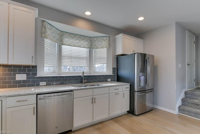 kitchen with light stone countertops, appliances with stainless steel finishes, white cabinetry, light hardwood / wood-style floors, and sink