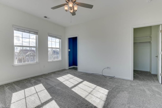 unfurnished bedroom featuring ceiling fan, a closet, a walk in closet, and dark colored carpet