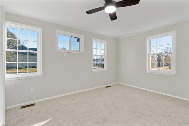 unfurnished room featuring a wealth of natural light, light carpet, crown molding, and ceiling fan