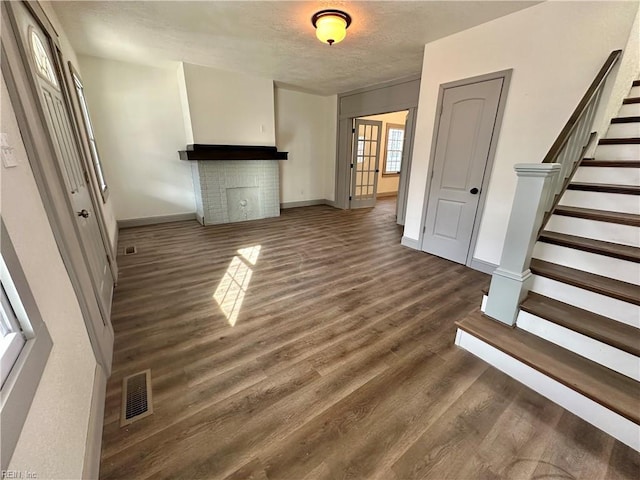 unfurnished living room featuring dark wood-type flooring and a brick fireplace