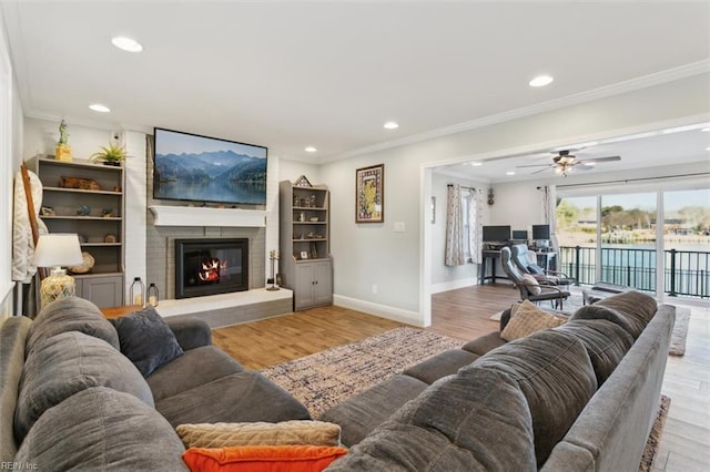 living room with light hardwood / wood-style floors, a brick fireplace, ceiling fan, and ornamental molding