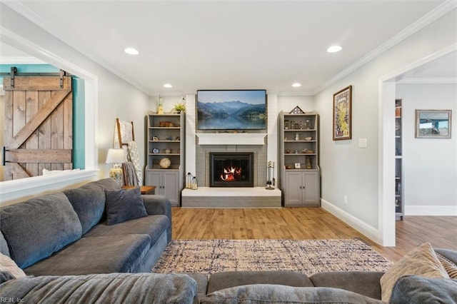 living room with a barn door, crown molding, light hardwood / wood-style floors, and a brick fireplace