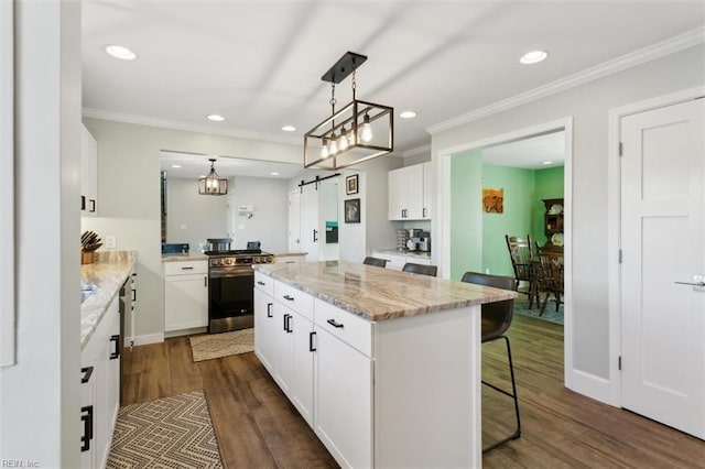 kitchen with white cabinets, a barn door, decorative light fixtures, a kitchen island, and stainless steel range oven