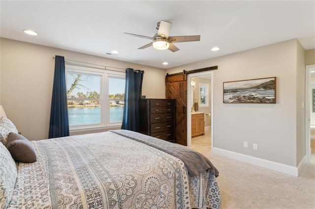 bedroom with ceiling fan, a barn door, ensuite bathroom, light colored carpet, and a water view