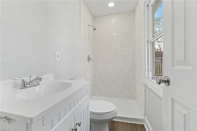 bathroom with tiled shower, hardwood / wood-style floors, vanity, and toilet