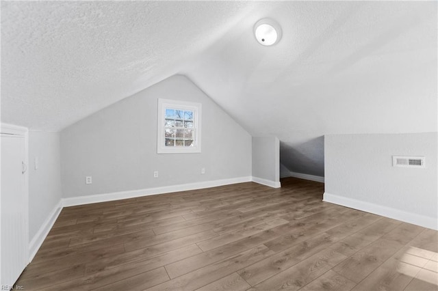 additional living space with a textured ceiling, dark hardwood / wood-style flooring, and lofted ceiling