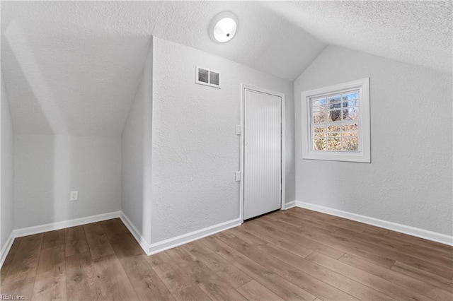 bonus room with a textured ceiling, hardwood / wood-style flooring, and vaulted ceiling