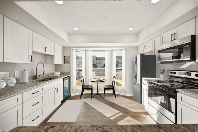 kitchen with white cabinets, sink, light hardwood / wood-style flooring, appliances with stainless steel finishes, and light stone counters