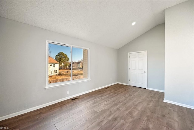 unfurnished room with hardwood / wood-style flooring, a textured ceiling, and vaulted ceiling