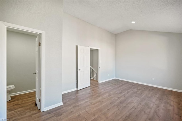 unfurnished bedroom with a textured ceiling, connected bathroom, lofted ceiling, and hardwood / wood-style floors