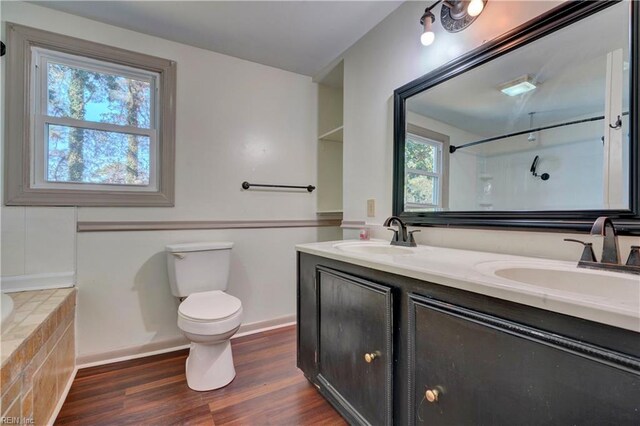 bathroom with hardwood / wood-style floors, vanity, a relaxing tiled tub, and toilet