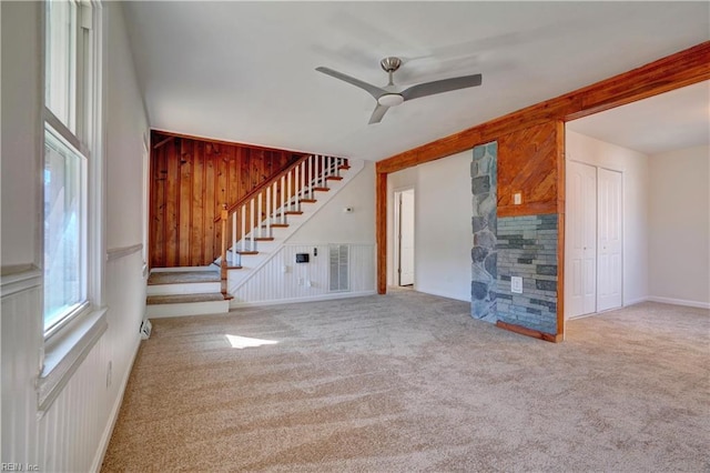 unfurnished living room featuring ceiling fan, light colored carpet, and wooden walls