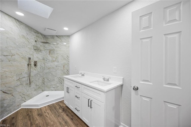 bathroom with a tile shower, a skylight, hardwood / wood-style floors, and vanity