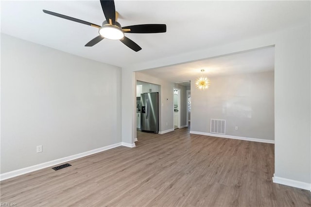 unfurnished room featuring ceiling fan with notable chandelier and light wood-type flooring