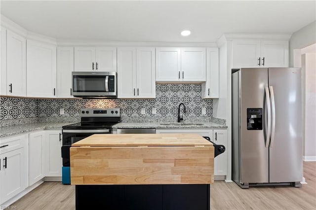 kitchen with white cabinets, sink, appliances with stainless steel finishes, a kitchen island, and light stone counters