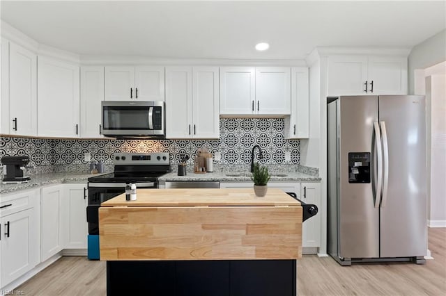 kitchen featuring white cabinets, light wood-type flooring, appliances with stainless steel finishes, a kitchen island, and light stone counters